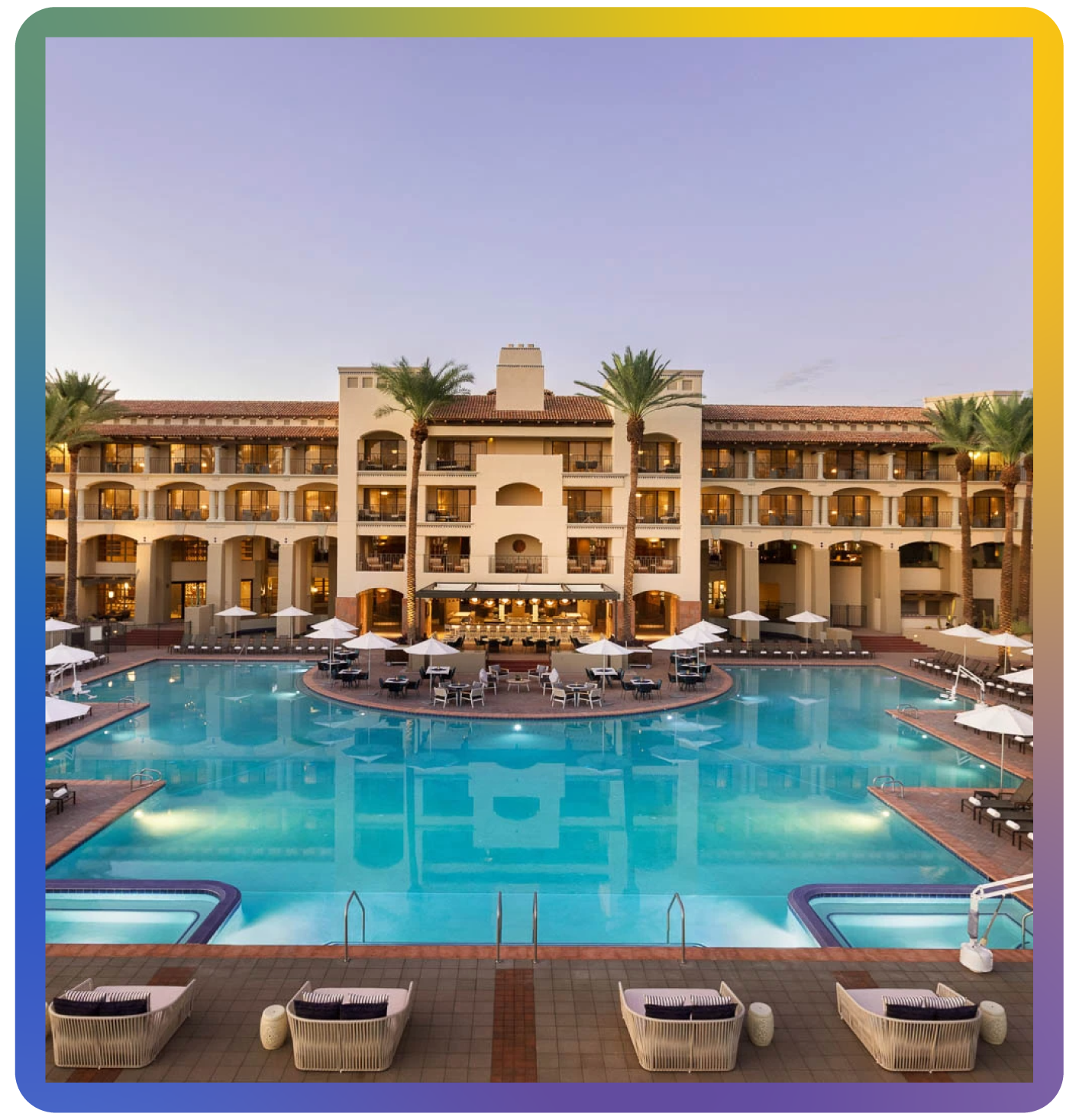 The luxurious Fairmont Scottsdale Princess resort, site of Language Is Limitless:TNI 2025 conference, featuring a large illuminated swimming pool surrounded by sun loungers and umbrellas. The multi-story building, with palm trees and balconies, stands in the background under a clear evening sky.