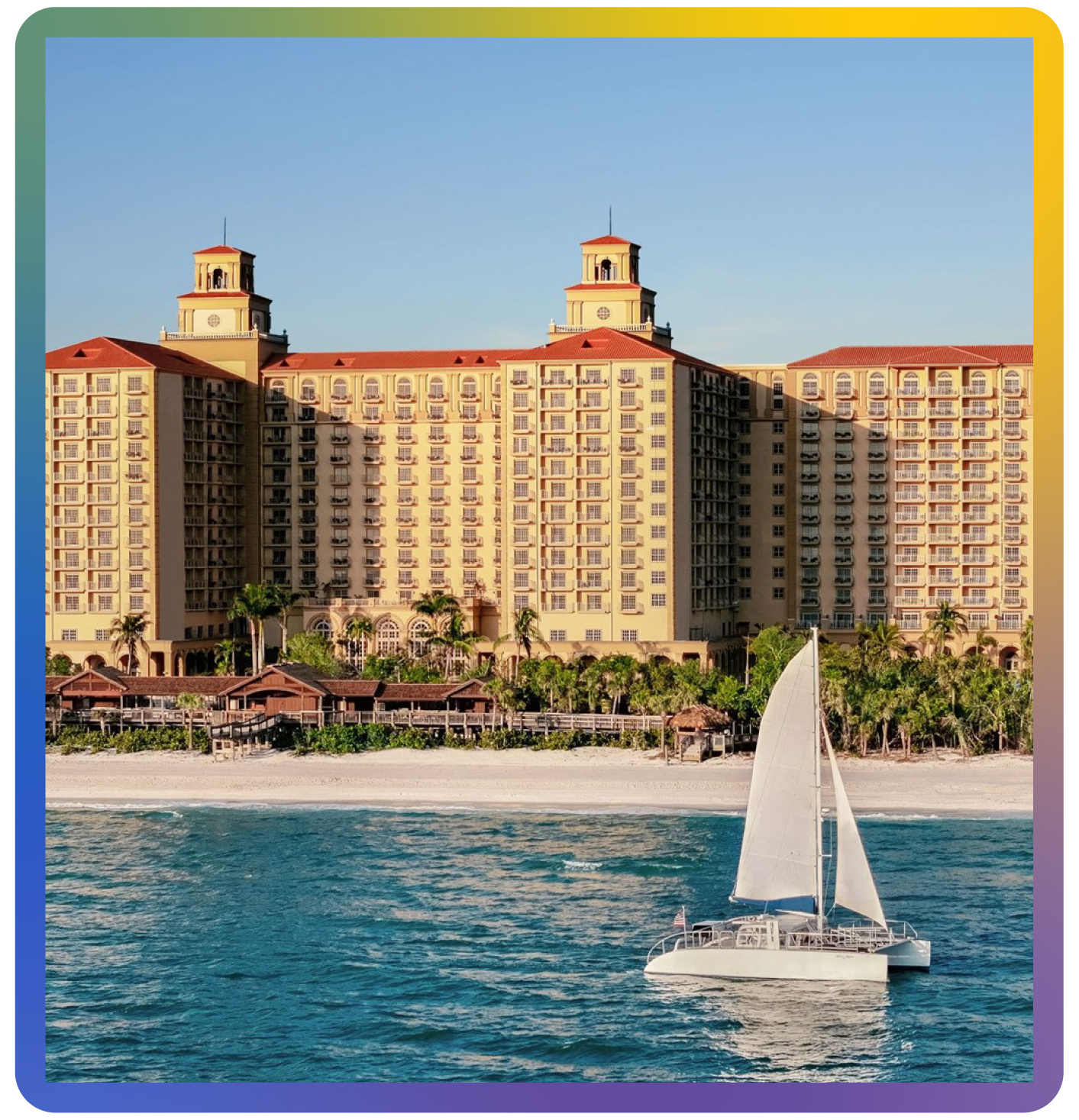 A sailboat glides across the bright blue ocean in front of the Ritz-Carlton, Naples resort, site of the Leadership In Action TNI conference. The resort features multiple floors and towers, with palm trees lining the sandy beach. The sky is clear and sunny.